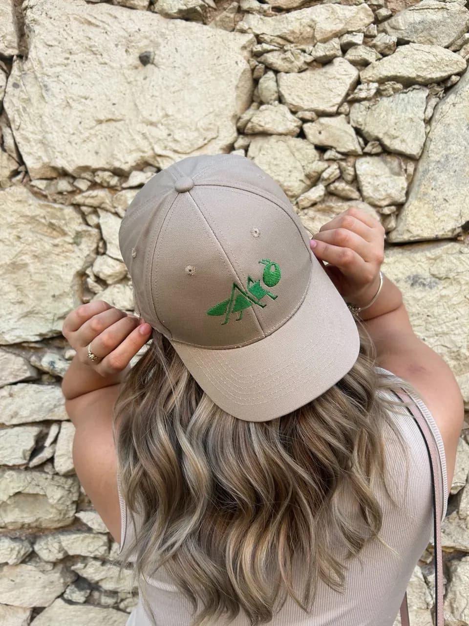 Modelo mostrando una gorra bordada frente a un muro de piedra